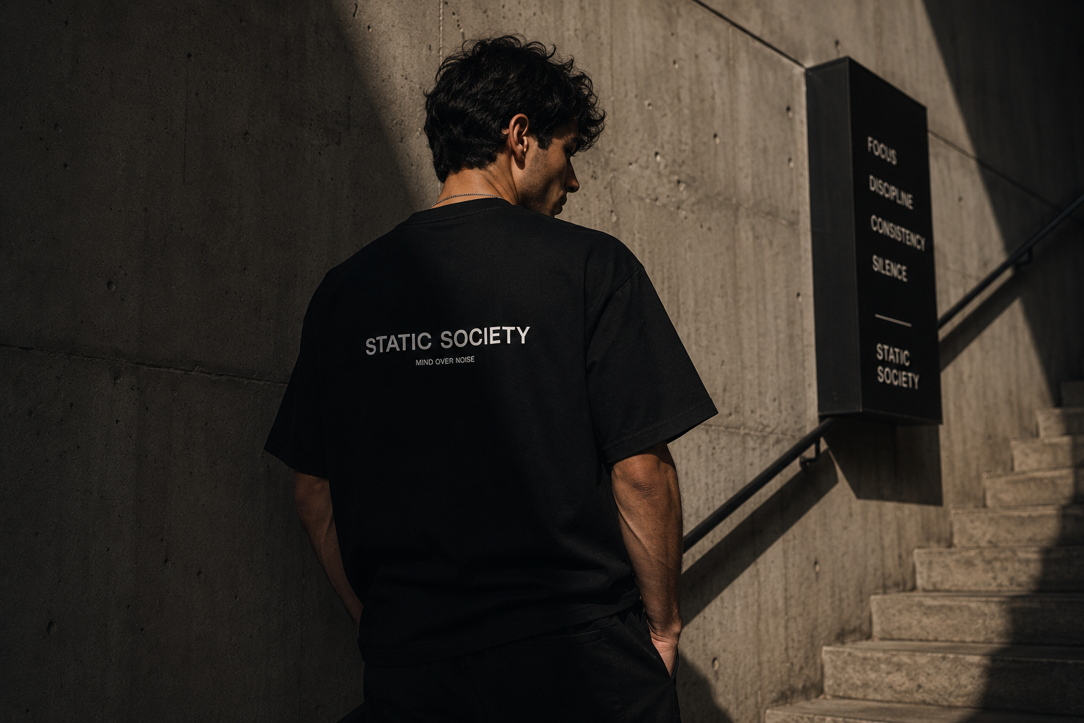 Static Society — back print tee beside brand signage, daylight stairs